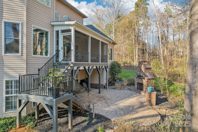 view of patio featuring fence, an outdoor stone fireplace, stairs, and a sunroom