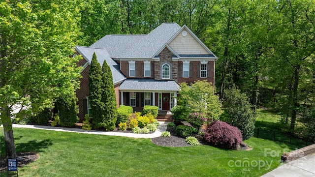 craftsman inspired home with brick siding, roof with shingles, a porch, and a front yard