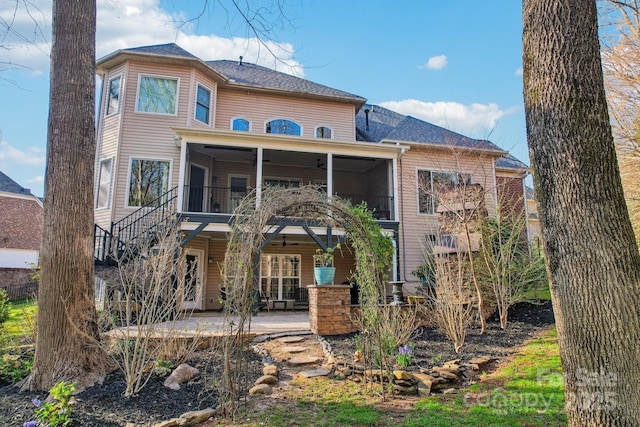 rear view of house featuring stairway, a patio area, a shingled roof, and a sunroom