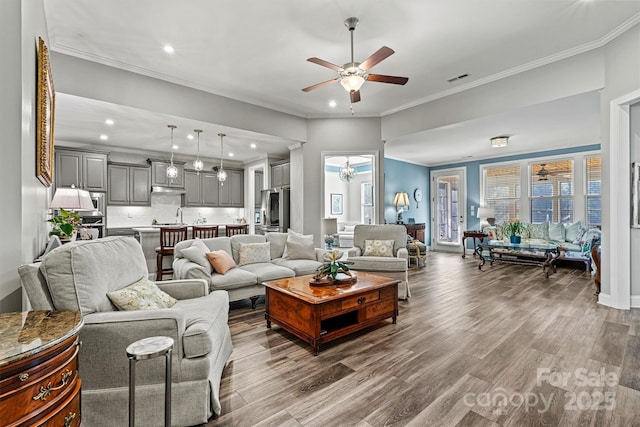 living area with visible vents, wood finished floors, a ceiling fan, and ornamental molding