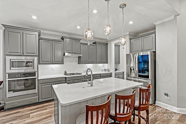 kitchen with crown molding, under cabinet range hood, decorative backsplash, gray cabinets, and stainless steel appliances