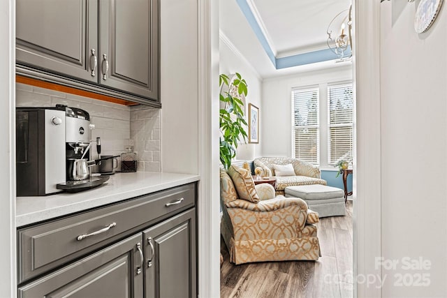 bar featuring tasteful backsplash, wood finished floors, a raised ceiling, and ornamental molding