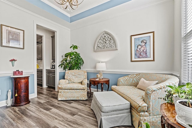 living area with crown molding, baseboards, a chandelier, wood finished floors, and a raised ceiling