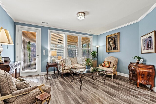 sitting room featuring baseboards, wood finished floors, visible vents, and ornamental molding