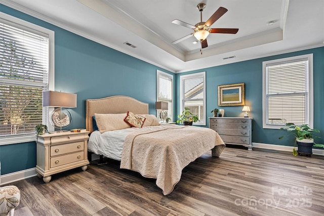 bedroom with visible vents, a tray ceiling, wood finished floors, crown molding, and baseboards