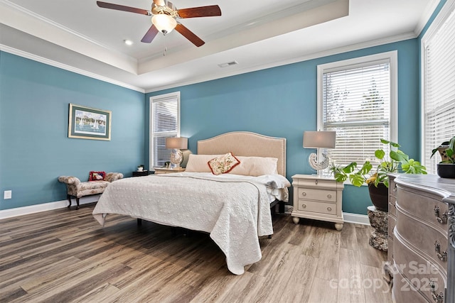 bedroom with baseboards, crown molding, a tray ceiling, and wood finished floors