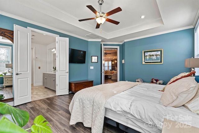 bedroom featuring visible vents, wood finished floors, connected bathroom, crown molding, and a raised ceiling