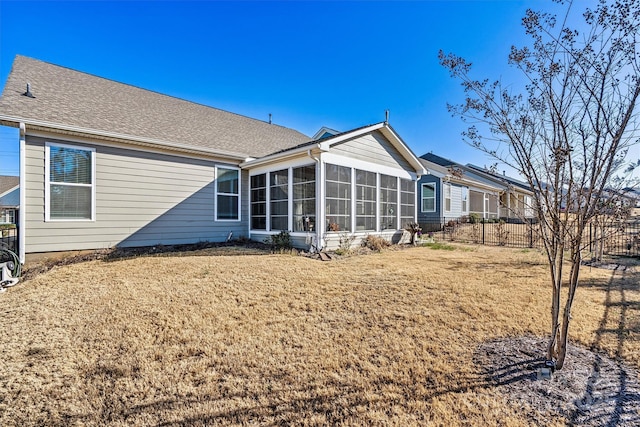 rear view of property featuring a lawn, fence, and a sunroom