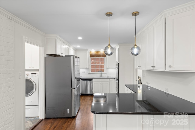 kitchen featuring a sink, dark countertops, appliances with stainless steel finishes, a peninsula, and washer / dryer