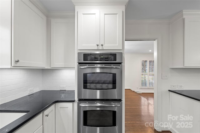 kitchen featuring backsplash, crown molding, wood finished floors, stainless steel double oven, and white cabinets