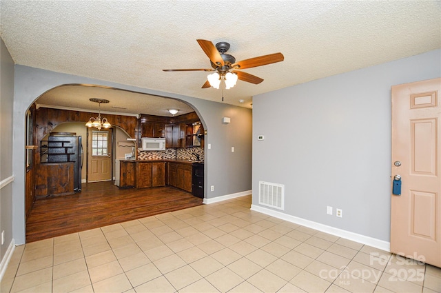 kitchen featuring white microwave, visible vents, light tile patterned floors, ceiling fan with notable chandelier, and arched walkways