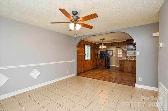 spare room featuring visible vents, ceiling fan with notable chandelier, light tile patterned flooring, arched walkways, and a textured ceiling