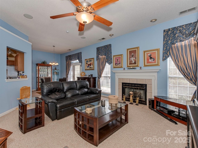 carpeted living room featuring baseboards, visible vents, a tile fireplace, a textured ceiling, and ceiling fan with notable chandelier