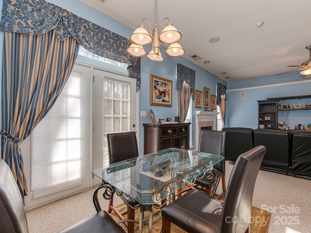 carpeted dining space featuring ceiling fan with notable chandelier, a fireplace, and visible vents