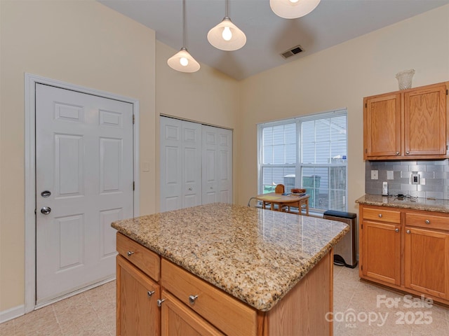 kitchen with visible vents, tasteful backsplash, a center island, light stone countertops, and hanging light fixtures