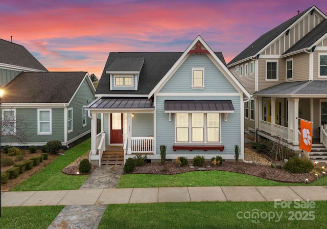 view of front of home with roof with shingles, a standing seam roof, a yard, covered porch, and metal roof