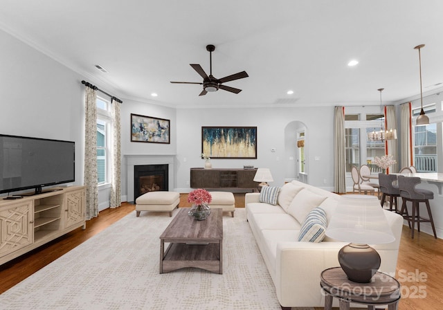 living room featuring arched walkways, visible vents, a glass covered fireplace, and wood finished floors