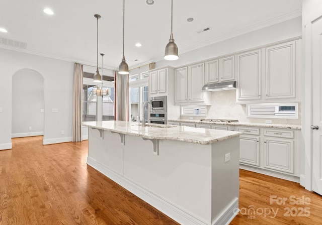 kitchen featuring under cabinet range hood, arched walkways, stainless steel appliances, and light wood-style floors