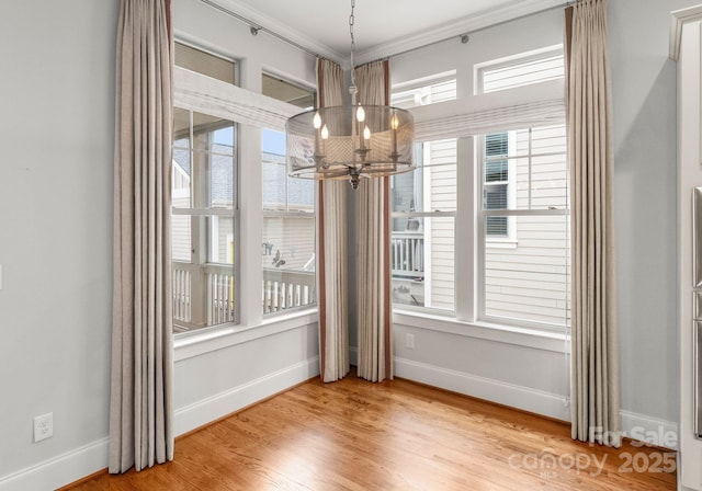 unfurnished dining area featuring a notable chandelier, wood finished floors, baseboards, and ornamental molding