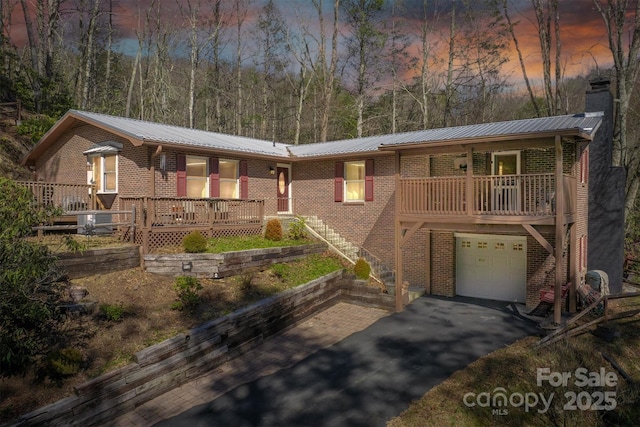 view of front of house with driveway, an attached garage, metal roof, brick siding, and a chimney