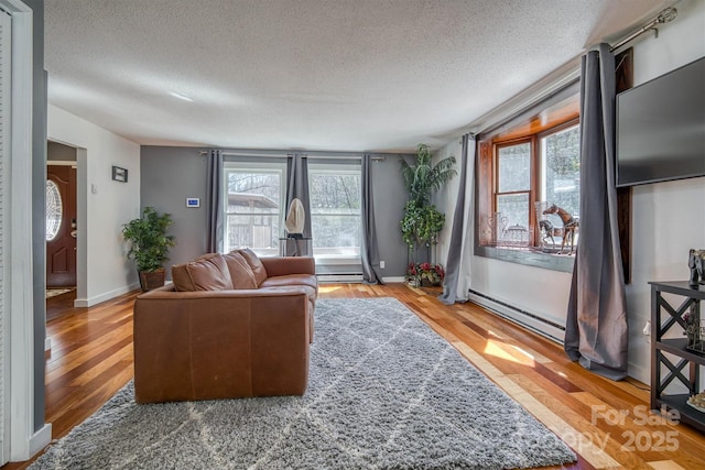 living room featuring a baseboard radiator, baseboards, a textured ceiling, and wood finished floors