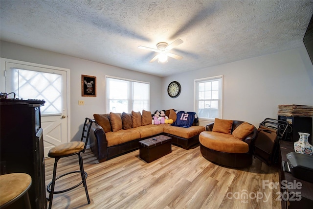 living room featuring a ceiling fan, light wood-style floors, a wealth of natural light, and a textured ceiling