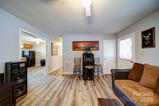 living room with visible vents, baseboards, ceiling fan, light wood-type flooring, and a textured ceiling