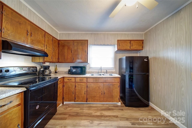 kitchen with under cabinet range hood, light countertops, brown cabinetry, black appliances, and a sink