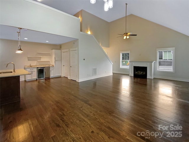 unfurnished living room featuring beverage cooler, a ceiling fan, a sink, dark wood-style floors, and a fireplace