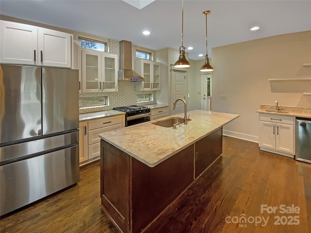 kitchen with dark wood-type flooring, wall chimney range hood, appliances with stainless steel finishes, and a sink