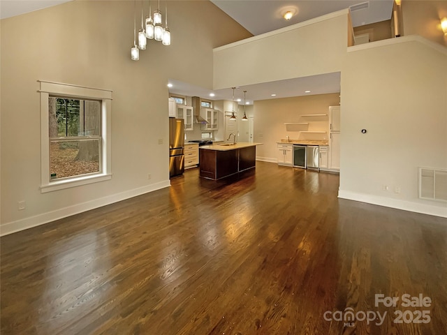 unfurnished living room featuring baseboards, visible vents, dark wood finished floors, an inviting chandelier, and a sink