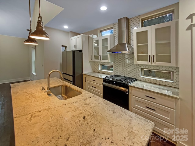 kitchen with tasteful backsplash, wall chimney range hood, freestanding refrigerator, black range with gas cooktop, and a sink