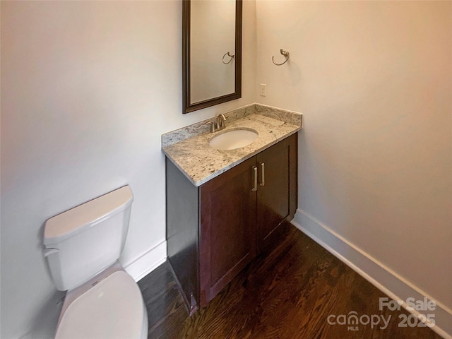 half bath with toilet, vanity, baseboards, and wood finished floors