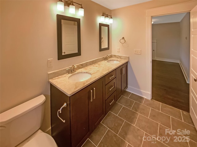 full bath with double vanity, toilet, baseboards, and a sink