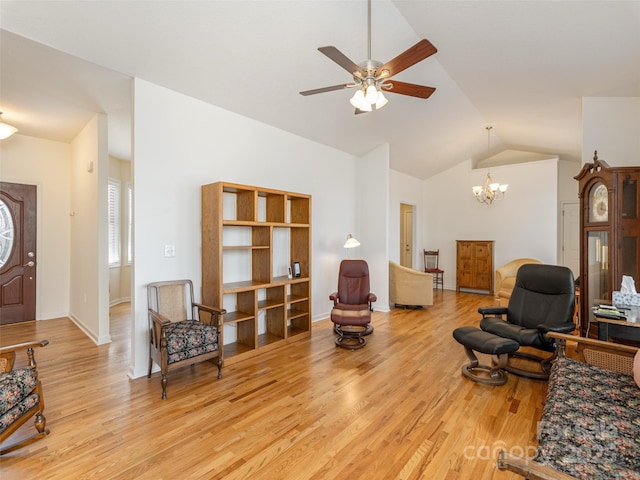 living area with ceiling fan with notable chandelier, light wood-type flooring, baseboards, and vaulted ceiling