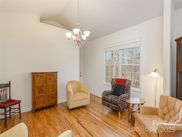 living area featuring a notable chandelier, light wood-style flooring, baseboards, and vaulted ceiling