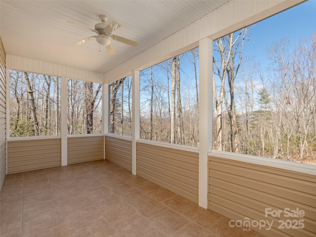 unfurnished sunroom featuring a wooded view and ceiling fan