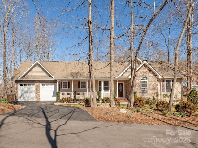 ranch-style house featuring aphalt driveway, brick siding, covered porch, and an attached garage