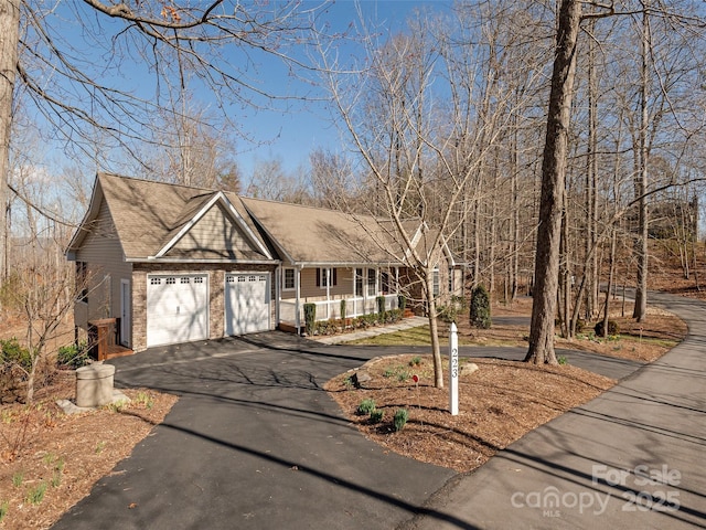 view of front of home with aphalt driveway, a porch, brick siding, and a garage