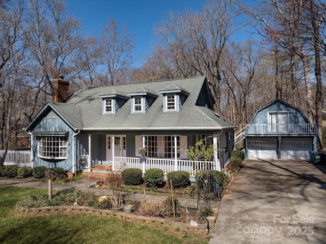 view of front of home featuring a shingled roof, covered porch, a chimney, a garage, and an outbuilding