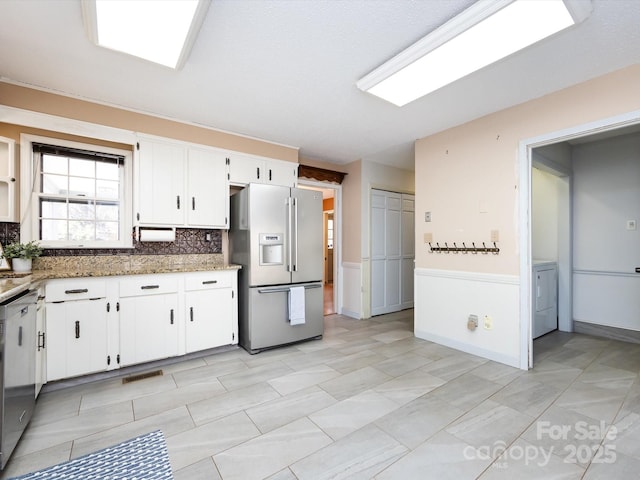 kitchen with visible vents, refrigerator with ice dispenser, light stone counters, white cabinets, and washer / dryer