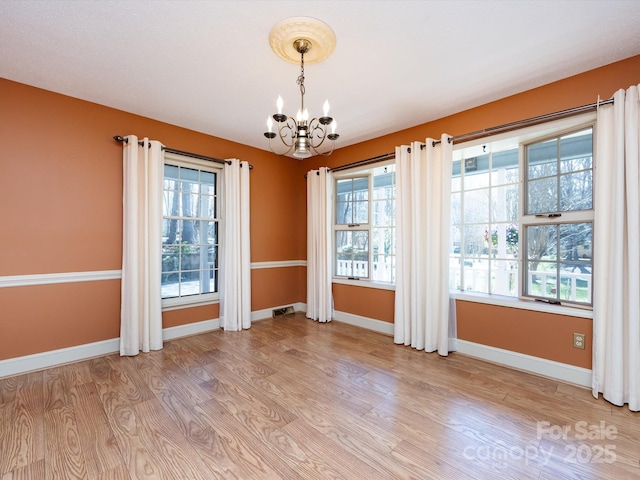 unfurnished dining area with light wood-type flooring, baseboards, a healthy amount of sunlight, and a chandelier