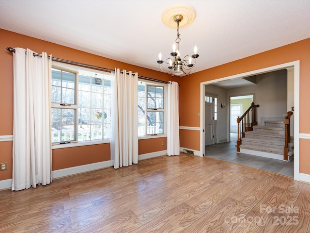 spare room featuring wood finished floors, plenty of natural light, and a chandelier