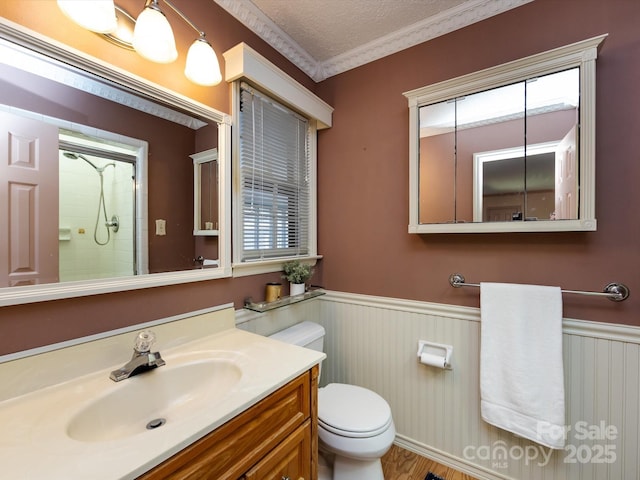 bathroom with toilet, a textured ceiling, wainscoting, walk in shower, and vanity