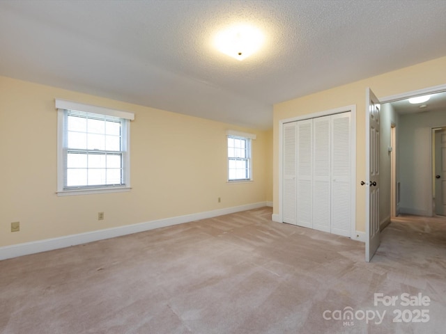 unfurnished bedroom with baseboards, light colored carpet, a closet, and a textured ceiling