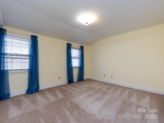 spare room with light carpet, a textured ceiling, baseboards, and vaulted ceiling