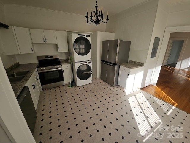 kitchen with appliances with stainless steel finishes, white cabinetry, an inviting chandelier, and stacked washer and dryer