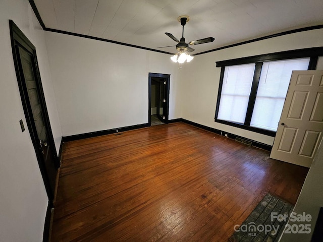 spare room with dark wood-type flooring, a ceiling fan, baseboards, and ornamental molding