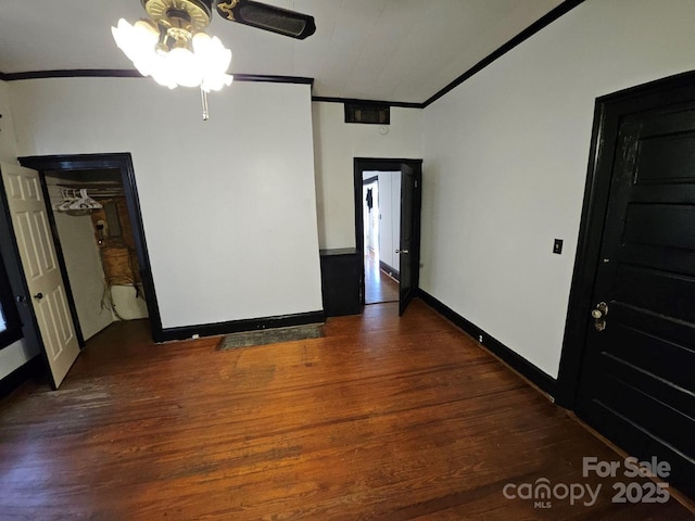 empty room with crown molding, baseboards, and dark wood-type flooring