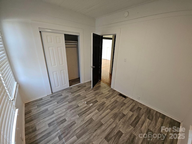 unfurnished bedroom with wood finished floors, visible vents, and a closet